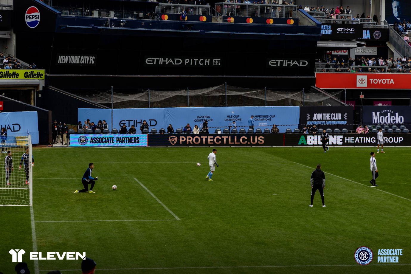 Yankee Stadium pitch with NYCFC players warming up and PROTECTLLC.US LED signage